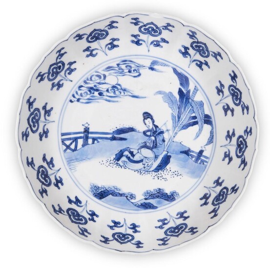 A Chinese blue and white dish, Kangxi period, painted to the central reserve with a lady seated in a garden landscape beside a banana tree beneath the moon emerging from clouds, inside a stylised floral border, apocryphal underglaze blue six...