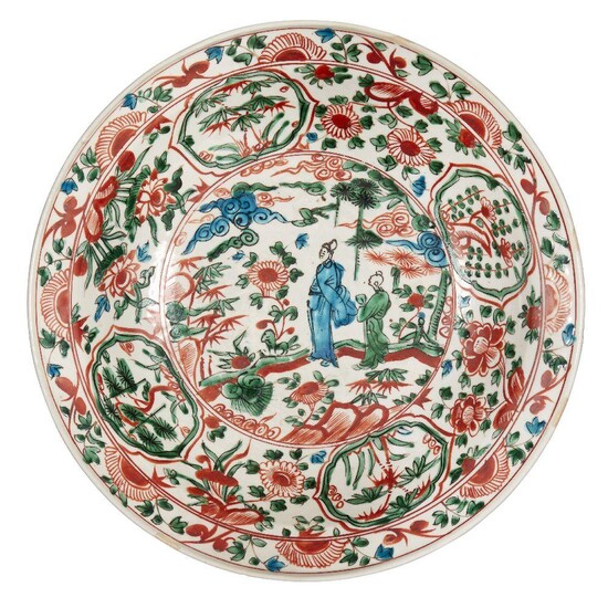 A large Chinese Zhangzhou ware charger, 16th century, painted in red, green and turquoise enamels with a scholar and attendant in a garden landscape filled with pine and bamboo, surrounded by flowering daisy and chrysanthemum blossoms, the sky...