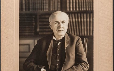 Edison, Thomas Alva (1847-1931) Signed Photograph. Black-and-white photograph of Edison in his suit, seated in a library, hands folded