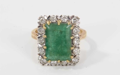 Emerald and diamond cluster ring with a rectangular step cut emerald measuring approximately 12.85mm x 8.75mm x 5mm, surrounded by a border of brilliant cut diamonds in claw setting on 18ct gold sh...