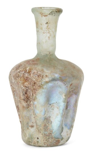 A Roman glass vessel, Rhineland, circa 3rd-4th century AD., with rounded shoulders and tapering cylindrical body, the sides with indentations or fluting on the body, with tall cylindrical neck and slightly flared rim, 14cm. high Provenance Mr...