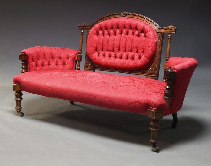 A Victorian walnut framed sofa, the carved back panel with oval upholstered backrest, flanked by curved sides, upholstered in crimson Damask pattern fabric, on front turned and fluted legs with castors