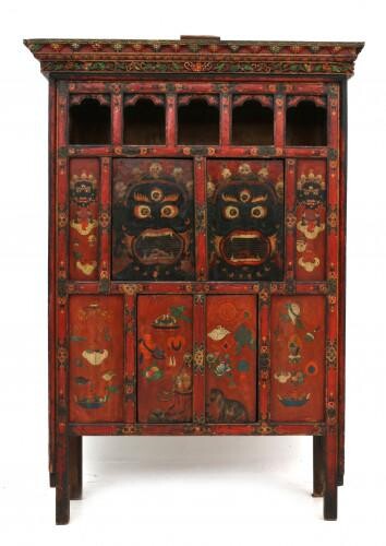 A painted wooden cabinet, the front with four doors and an open gallery running along the top. Decorated with precious objects and Bhairab masks. Tibet, 19/20th century.