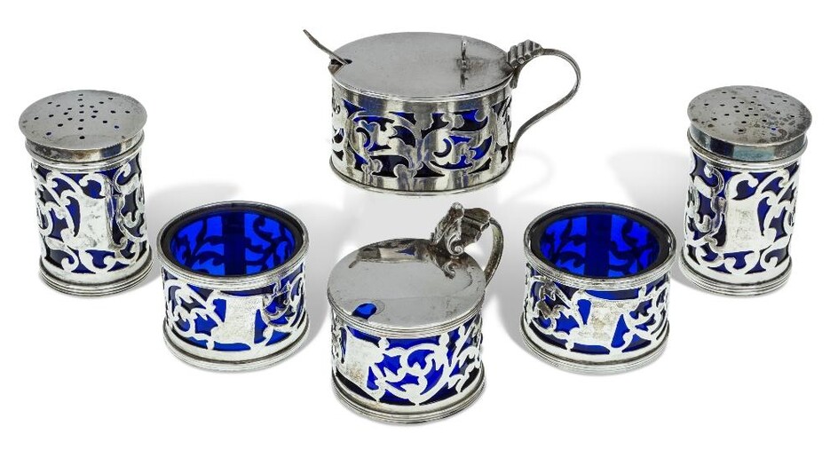 An Edwardian silver cruet set, Birmingham, 1904, Martin Hall & Co., designed with pierced sides and blue glass liners, the set comprising two salts, two peppers and a mustard, together with a matched mustard of similar design, Birmingham, 1907...