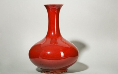 A CHINESE COPPER RED-GLAZED BOTTLE VASE. Qing Dynasty. With a compressed globular body sweeping up to a tall cylindrical neck with a flared mouth, all supported on a short foot, covered overall in a thick deep copper-red glaze, the interior and the...