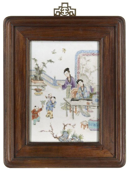 A Chinese porcelain famille rose plaque, 19th century, painted with two ladies in traditional dress, one sat at a table with a guqin and various scholar's objects, the other stood watching three boys playing in a garden, decorated with jardinières...