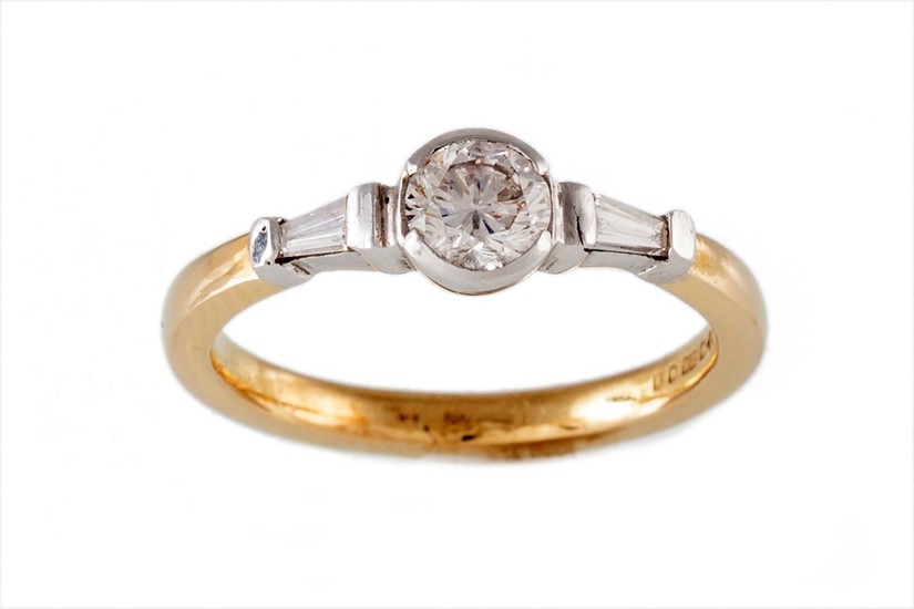 A SOLITAIRE DIAMOND RING, flanked by tapered baguette cut di...