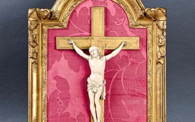 ** Crucifix en ivoire sculpté, le Christ au périzonium noué à droite, sur fond de tissu rouge, dans un encadrement en bois sculpté et doré du XVIIIe siècle
