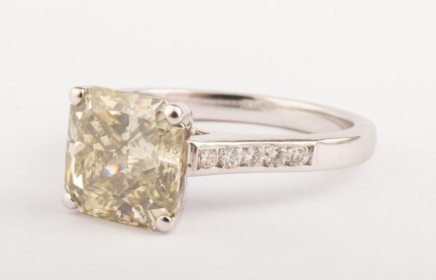 Ring in 18k white gold (750 thousandths) surmounted by a 2.64 ct. yellow diamond with a slight greyish tinge, radiant cut, SI2 quality. On the shoulders of the ring, two lines of five small round brilliant diamonds for about 0.30 ct. Very bright stone.