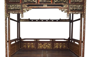 A Chinese four-poster bed, jia zi chuang, early 20th century, standing on lacquered and gilt painted feet in form of scrolling foliage, the frame supports four square posts to each corner and two additional posts to each side atop the canopy frame...