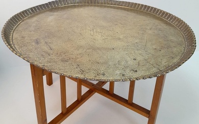 A MIDDLE EASTERN BRASS TOPPED TABLE WITH FOLDING WOODEN LEGS...