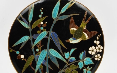 A large Minton's Kensington Art Pottery Studio wall charger, in the manner of Dr Christopher Dresser, the design depicting a bird flying past bamboo shoots, in colours on a black ground, outlined in gilt and imitating Japanese cloissone enamel...
