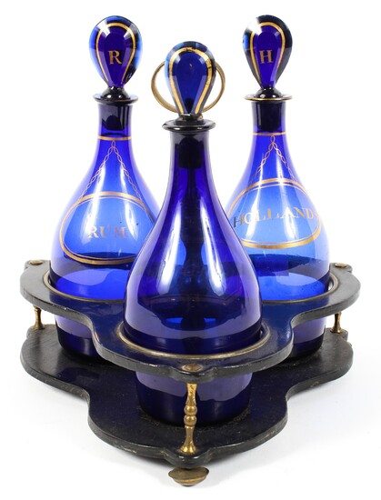 A set of three Regency Bristol blue glass spirit decanters in a papier-mache and brass stand