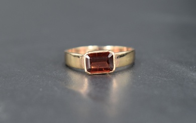 A yellow metal band ring having an inset baguette cut red/orange stone, possibly a garnet