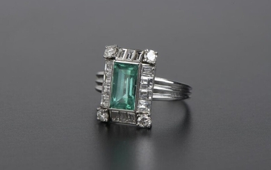 Ring in platinum 950 thousandths, the bezel set with a rectangular synthetic emerald in a setting of fourteen baguette-cut diamonds and four round brilliant cut diamonds.