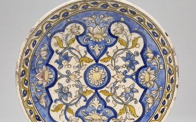 PLAT CREUX QÂJÂR en céramique peinte en polychromie sous glaçure incolore, d'une fleur épanouie centrale...