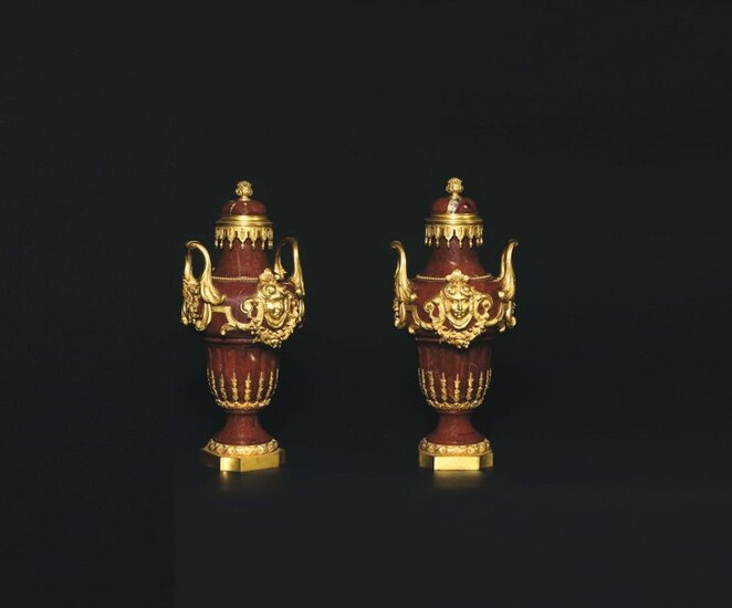 Pair of covered baluster-shaped vases in red marble, probably from Verona, decorated with a rich gilded bronze frame with a motif of female masks, with garlands of flowers held by the side handles ending with acanthus leaves. The neck is encircled by...
