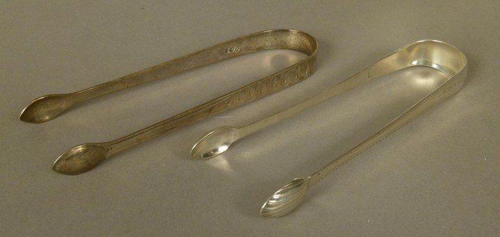 TWO GEORGE III SILVER SUGAR TONGS of bright cut decoration, ...