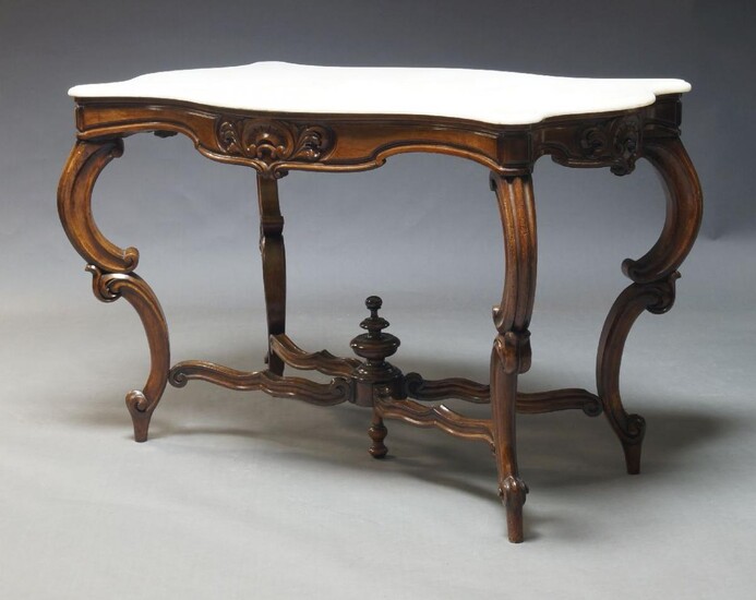 A French Louis XV style provincial centre table, early to mid 20th Century, the white marble top, of serpentine outline, above carved frieze on c-scroll supports united by x-shaped stretchers centred by turned finial, 83cm high, 125cm wide, 69cm deep