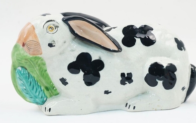 A Staffordshire pottery rabbit, mid to late 19th century, modelled with yellow eyes, black patches and ears, and eating a lettuce leaf, collector's label to underside, 25cm long