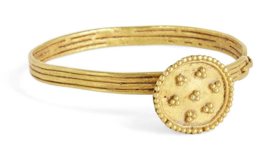 A gold bangle for a baby, Iran, 12-13th century, the band formed of four, wires soldered together, the raised bezel with disc face set with seven clusters of gold granules, hinge to one side, 4cm. diam.