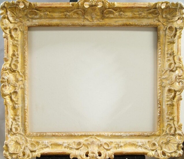 A Carved and Gilded Louis XIV Style Frame, late 20th century, with cavetto sight, stiff leaf course, sanded frieze, the plain hollow with foliate and flower head scrollwork, pierced cartouche centres and corners, and linked lozenge back edge, 58 x...