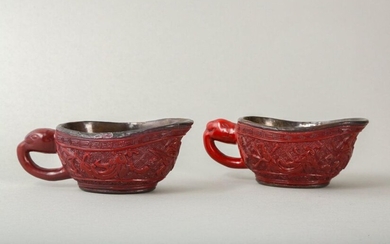 A PAIR OF CHINESE CINNABAR LACQUER POURING VESSELS, YI. Ming Dynasty, 15th Century. Of rounded elongated form supported on an oval foot, with a curved rim forming the spout on one side opposite a lion mask projecting a hoop handle, carved through the...