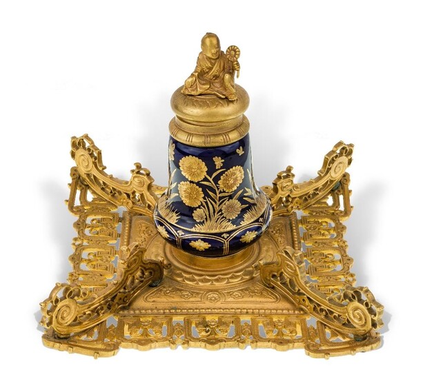 A Victorian gilt-bronze and porcelain inkwell, late 19th century, in the chinoiserie taste, the cover surmounted by a seated Chinaman, the inkwell decorated with flowers on a square pierced stand, the underside stamped REGISTERED, 14cm high, 17cm...