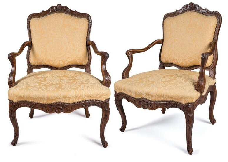 TWO FAUTEUILS with QUEEN REGENCE and LOUIS XV in moulded and richly carved natural wood, the backrests decorated with the cushioning of a flower. The moved armrests, one with a cuff, ending in scrolls with water and acanthus leaves that extend on...