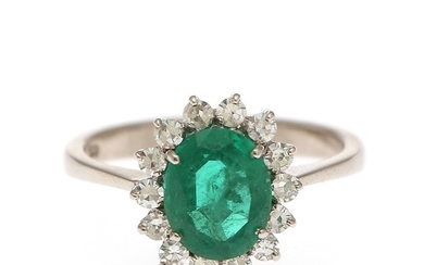 An emerald and diamond ring set with an oval-cut emerald encircled with numerous single-cut diamonds, mounted in 18k white gold. Size 58.5.