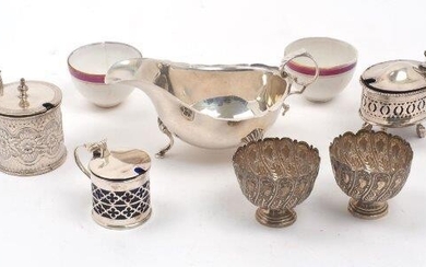A Victorian silver mustard, Birmingham, 1888, maker's mark rubbed, with floral motifs to body and fan thumbpiece to hinged cover, together with a further silver mustard, Chester, 1922, Haseler & Bill, with pierced quatrefoil design to blue glass...