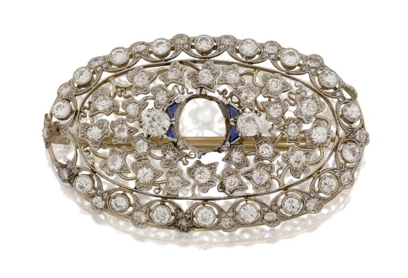 A diamond brooch, with central stone deficient, in the form of an oval pierced foliate panel set with old-brilliant-cut diamonds, one deficient, set with four calibre sapphires, approx. length 48cm(VAT charged on hammer price)