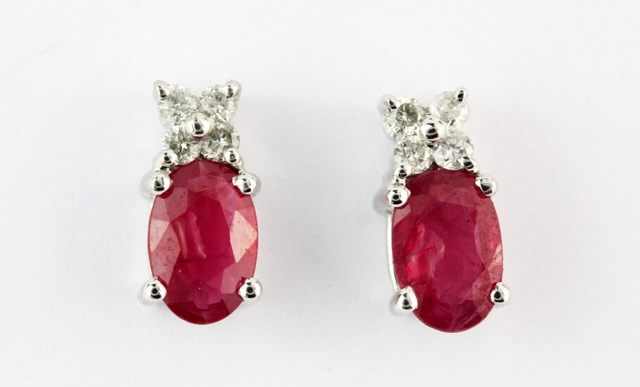 A pair of 9ct white gold (stamped 9k) stud earrings each set with an oval cut ruby and diamonds, L. 0.9cm.