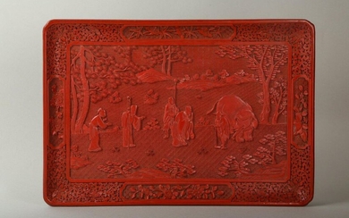 A CINNABAR LACQUERED ‘ELEPHANT’ TRAY. Qing Dynasty. Of rectangular form with canted corners the interior panel with an outdoor scene of figures bowing before the an elephant beside attendants, all within a floral borders each side centred by a panel...