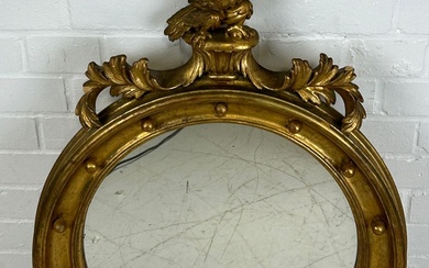 A GILT CIRCULAR WALL MIRROR WITH CARVED FRAME IN...