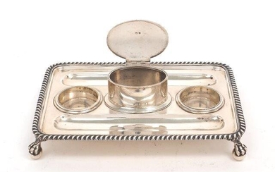 A George V silver inkstand, Birmingham, 1926, John Collard Vickery, the rectangular stand raised on four claw and ball feet to gadrooned border, the centre with oval compartment with hinged cover, inkwells deficient, 14.2 x 21cm long, approx...