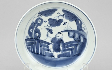 Assiette en porcelaine chinoise représentant un fou dans un jardin. 18e - 19e siècle. Marque...