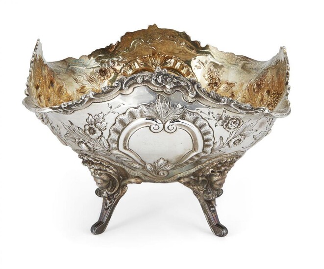 A Victorian silver fruit bowl with gilded interior, London, c.1899, Goldsmiths & Silversmiths Co., of shaped square form, the sides repousse decorated with baskets of flowers and fruit, vacant cartouches to two sides, the dish raised on four legs...
