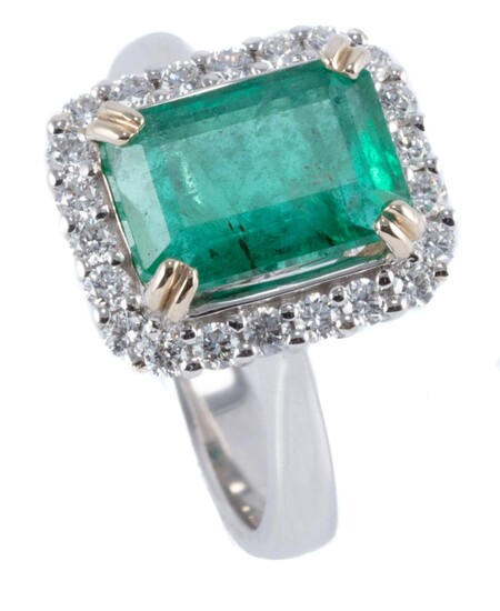 AN 18CT GOLD EMERALD AND DIAMOND RING; corner claw set with an emerald cut emerald of approx. 3.18ct surrounded by 22 round brillian...