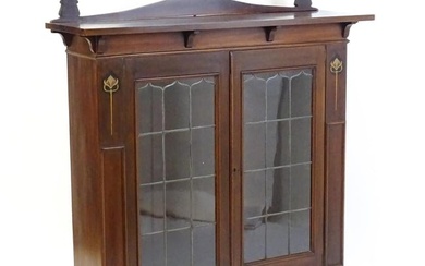 An Art Nouveau mahogany cabinet with a shaped upstand and two leaded glass doors with floral