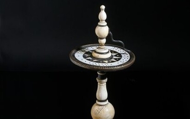 Table turnstile or roulette wheel in ivory and ebony veneer, the square top rests on four small raven feet, the turned shaft encircled by a revolving disc with inlaid dotted numbers designated by a bronze snake.