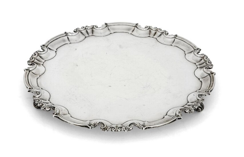 Two silver salvers, the larger example London, 1897, William Hutton & Sons, with shaped scroll and piecrust border, the base raised on three scroll feet, 30.5cm dia., the smaller salver with bead and foliate border, Sheffield, 1924, Travis, Wilson...