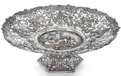 A Continental pierced centrepiece dish, possibly German, apparently unmarked, the pierced sides overlaid with floral swags and birds, the base designed with cherubic scene in relief, raised on a hexagonal pierced foot, 13cm high, 32.5cm dia.