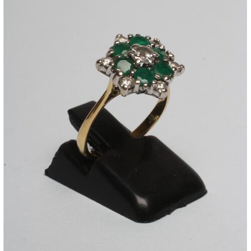 A DIAMOND AND EMERALD CLUSTER RING, the central diamond of a...