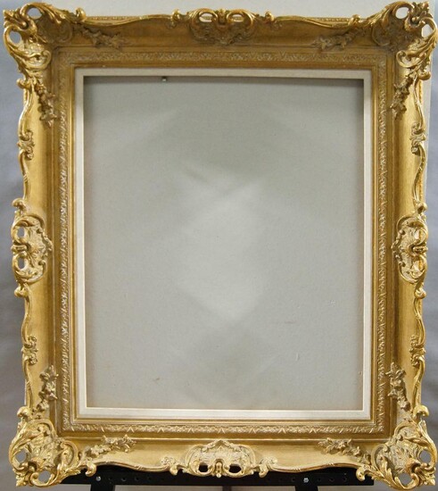 A Gilded Composition Louis XV Style Swept and Pierced Frame, late 20th century, with plain sight, stiff leaf course, the plain hollow with foliate and flower head scrollwork, shell cartouche centres and corners and schematic demi fleur back edge...
