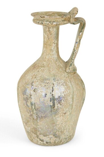 A Roman clear glass ewer, circa 1st-2nd century AD., the base with indented foot, globular ribbed body leading to a narrow neck widening at the rim, with a thick applied handle bending inwards at the rim, 15.5cm. high Provenance: Private family...