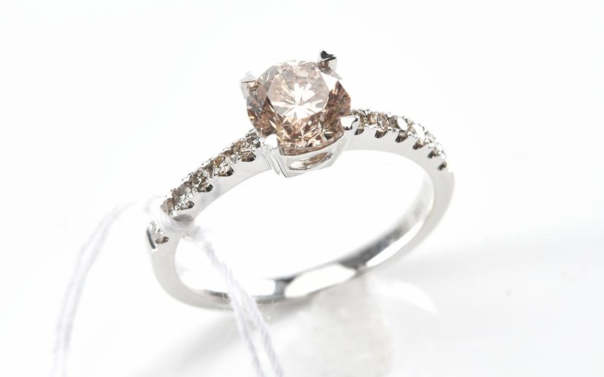 A SOLITAIRE DIAMOND RING - Featuring a round brilliant cut champagne diamond weighing 1.02ct to a diamond set band featuring twelve...