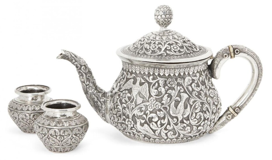 A silver repousse Kutch teapot, India, circa 1860 and two silver spice containers, of squat form with curved handle and spout, hinged domed lid with pinecone finial, the teapot handle with heat insulating discs of ivory, finely decorated to body...