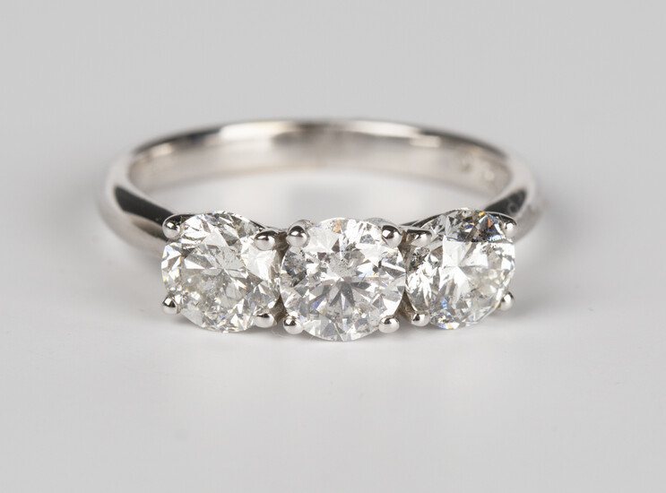 A white gold and diamond three stone ring, claw set with a row of circular cut diamonds, detailed