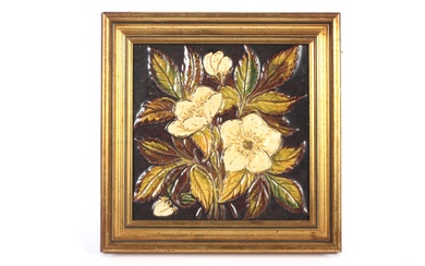 A framed Victorian relief-moulded glazed pottery tile. Decorated with a bouquet of white flowers and green leaves, reserved on a brown ground, within giltwood frame, 19cm square exc. frame